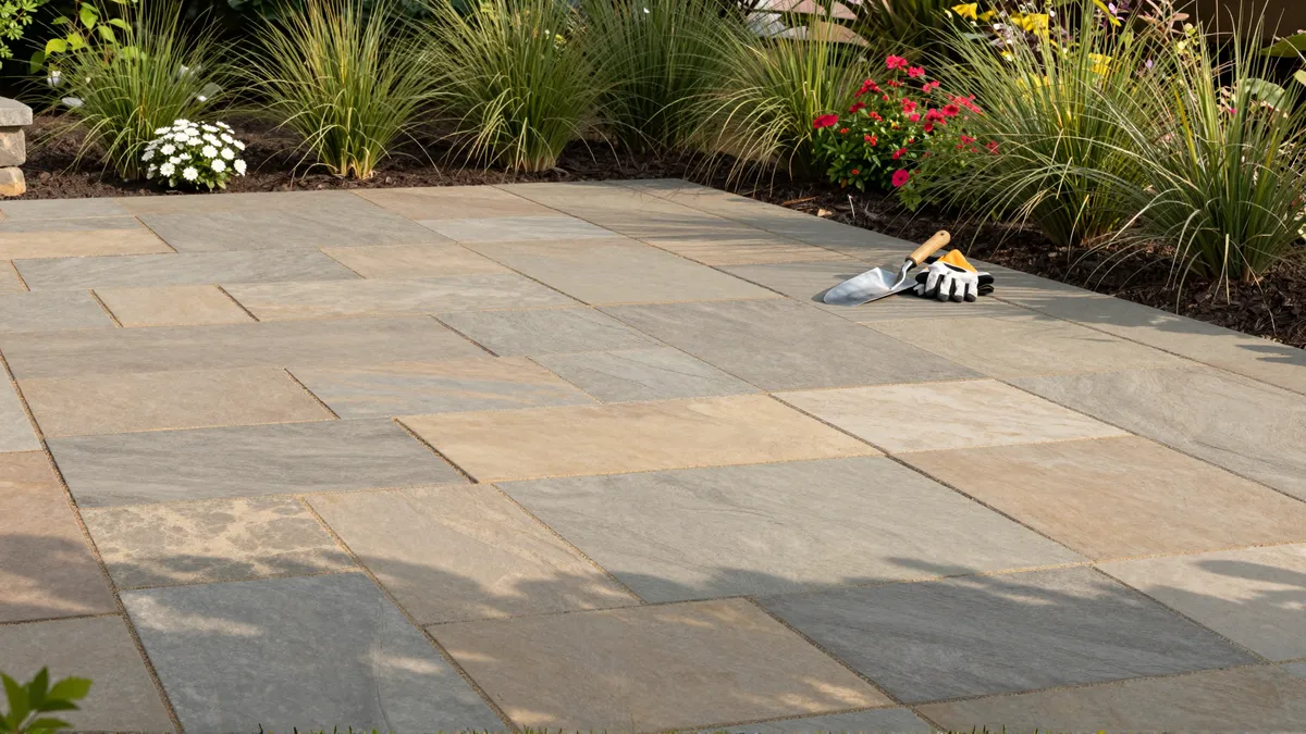Neu gebauter Sandstein-Patio mit Ziergräsern und Gartengeräten in der Morgensonne